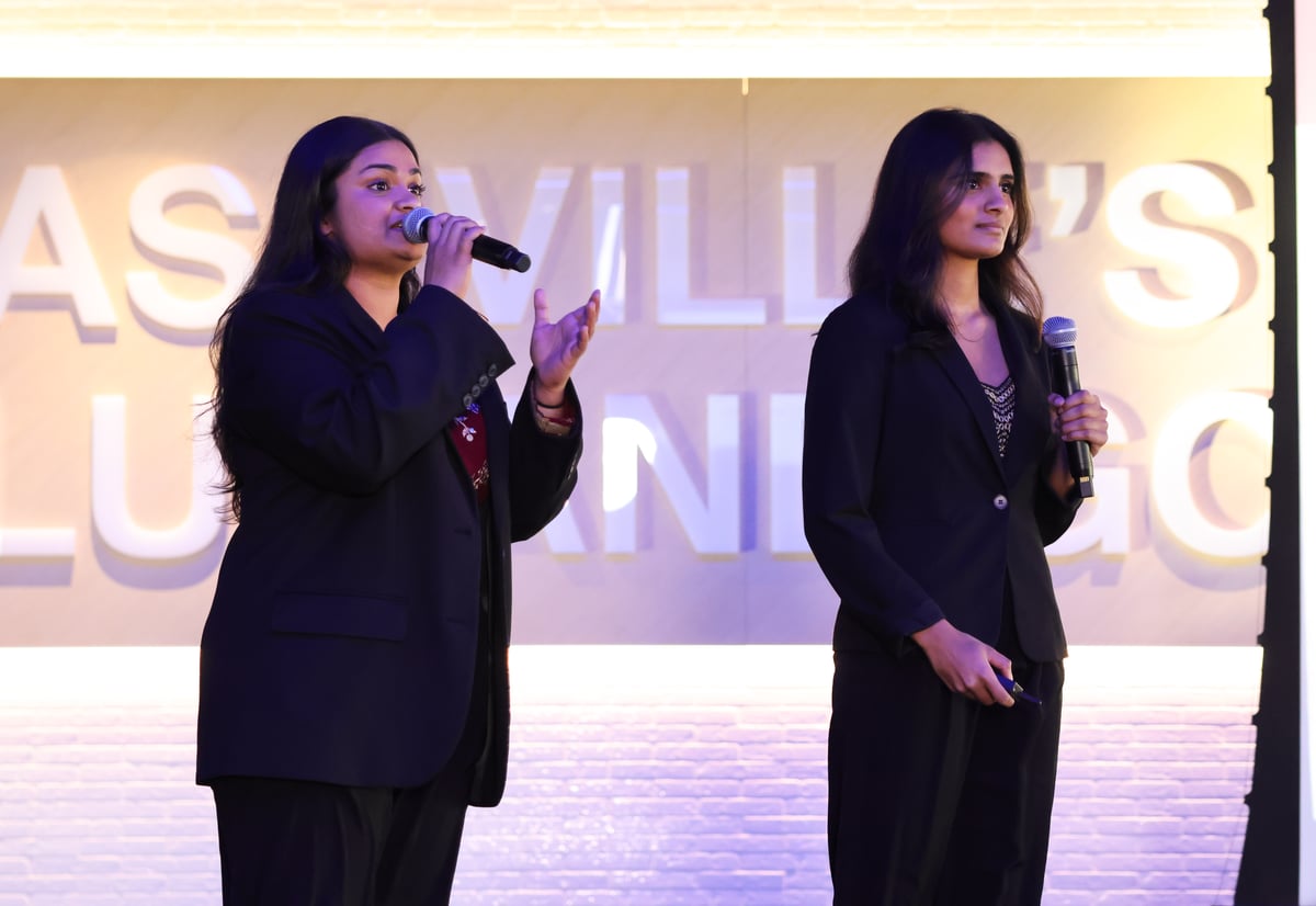 Two women in dark business suits standing on stage giving a presentation.